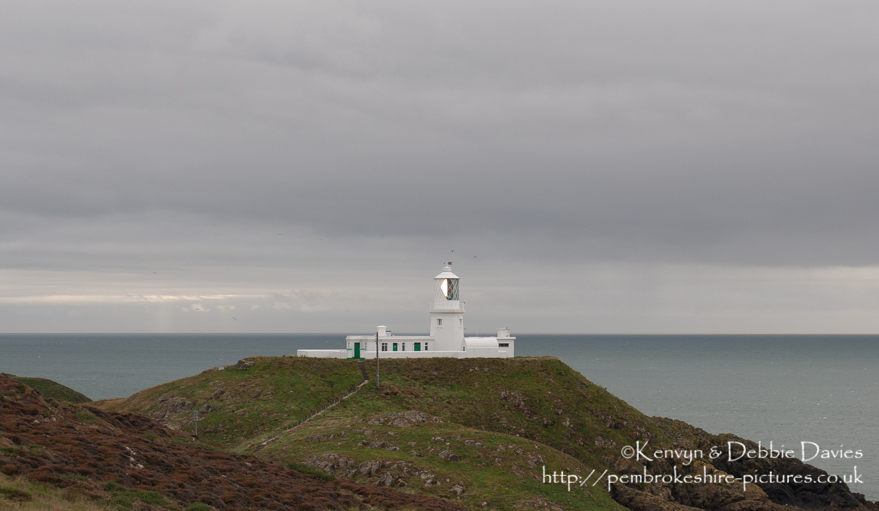 Strumble Head Lighthouse is built on Ynysmeicl (St. Michael's Island), an islet to the west of Fishguard, separated from the mainland by a very narrow gap.<br/><br/>The station was built in 1908 by Trinity House for the greater safety of sea traffic between Ireland and Fishguard Harbour which is located behind cliffs and a breakwater three miles to the east. The new light also formed a link with the existing South Bishop light, 18 miles to the south-west. This stretch of coast is very dangerous, and some 60 vessels are known to have been lost along it in the 19th Century alone.